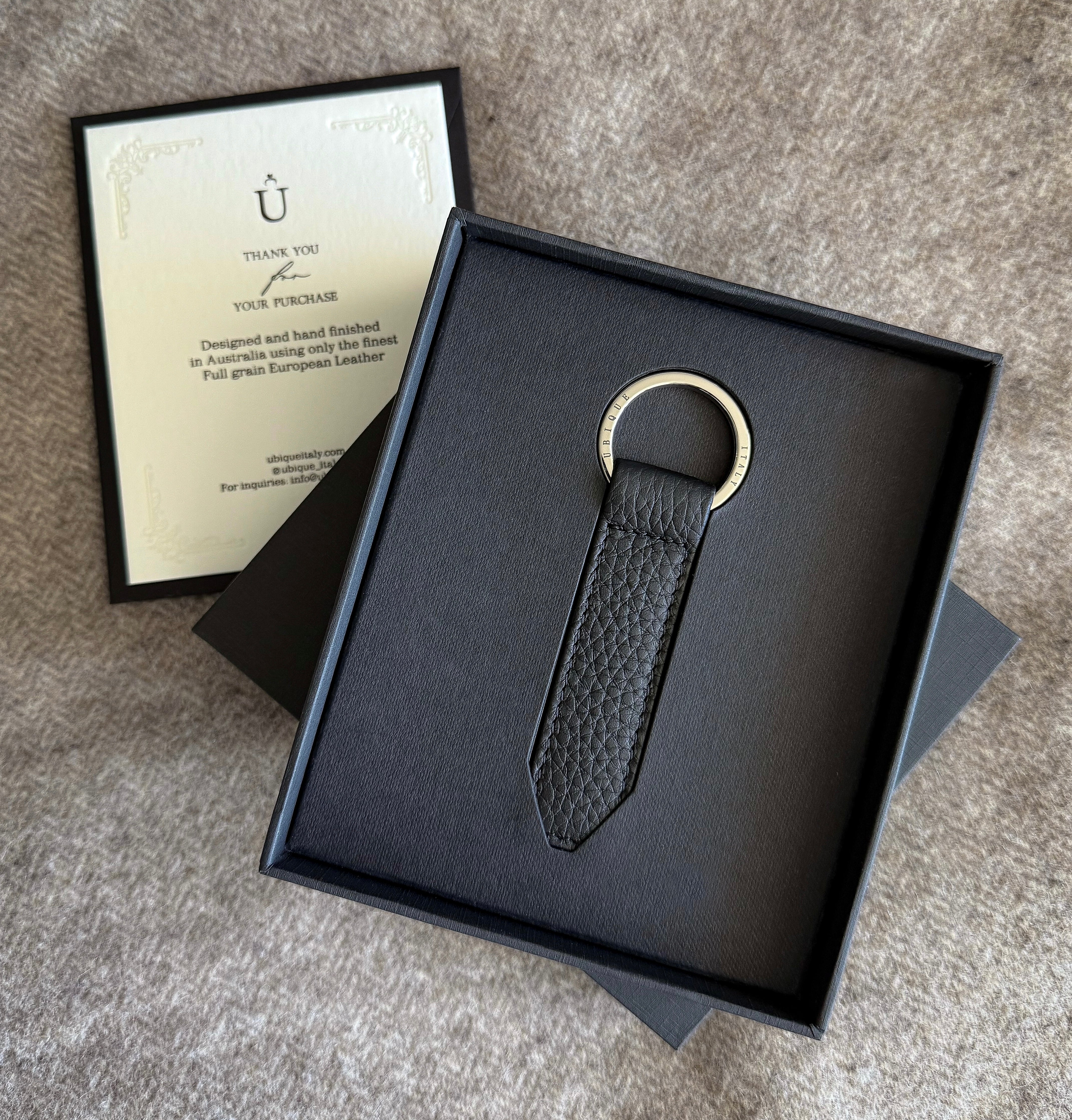 Black leather keychain in a black box with a card on a gray surface