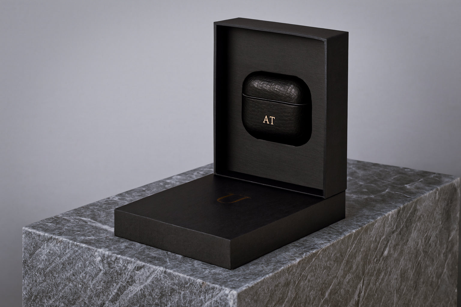 Black leather Airpod case with personalisation monogram in package on a gray stone surface