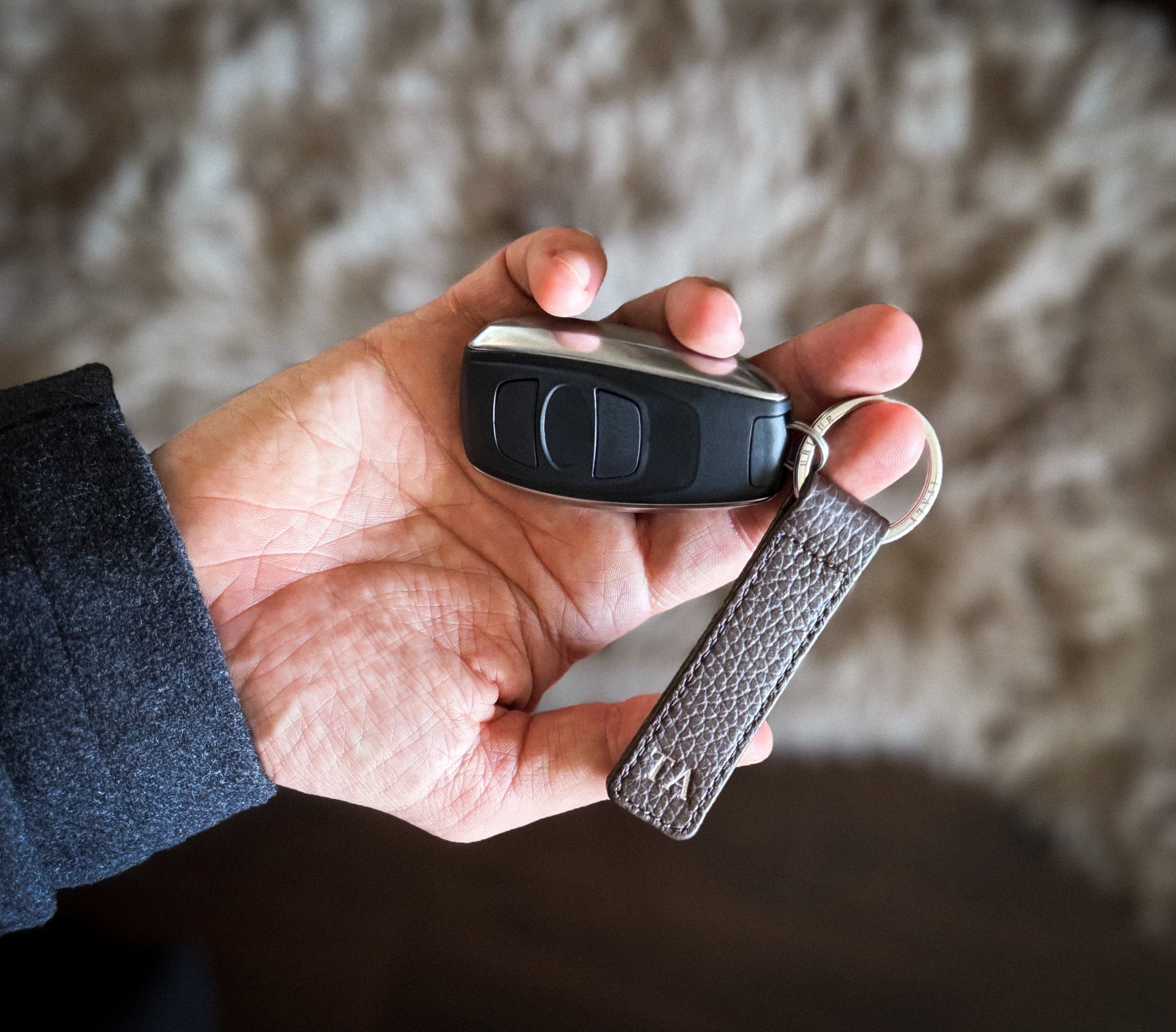Hand holding a car key fob with a leather keychain against a blurred background