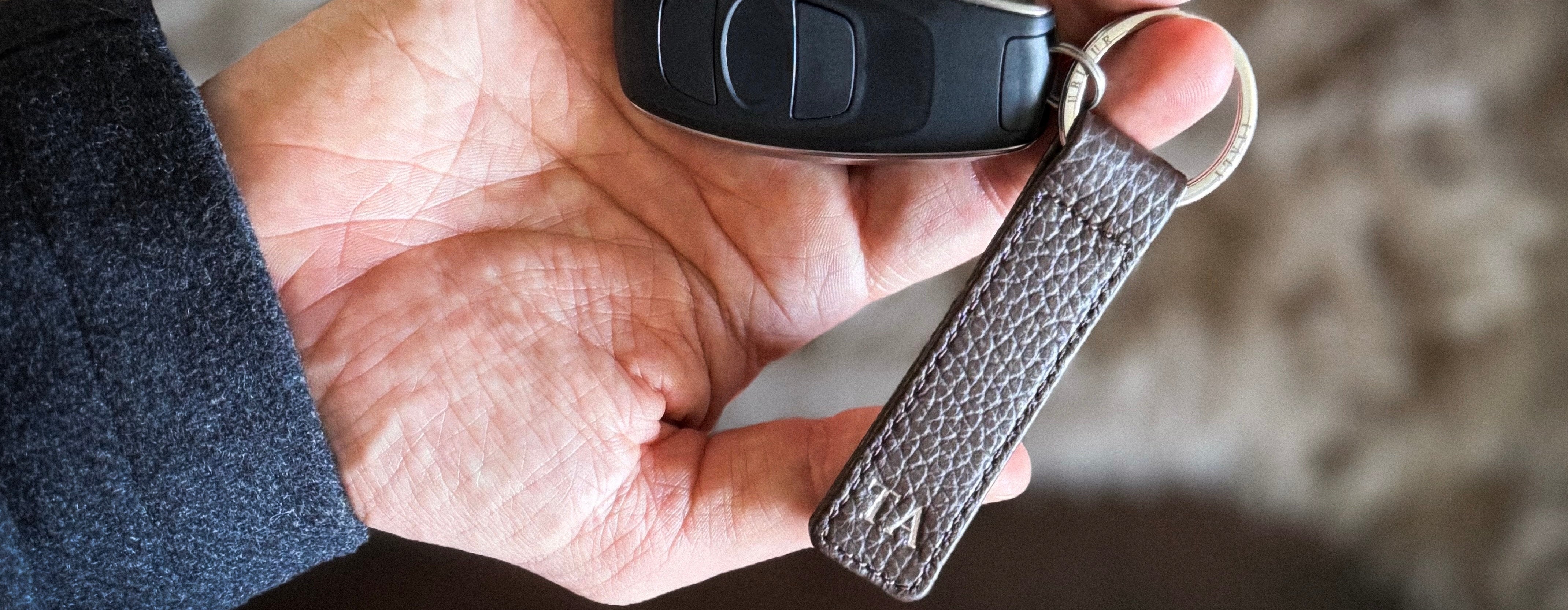 Hand holding a car key fob with a leather keychain against a blurred background