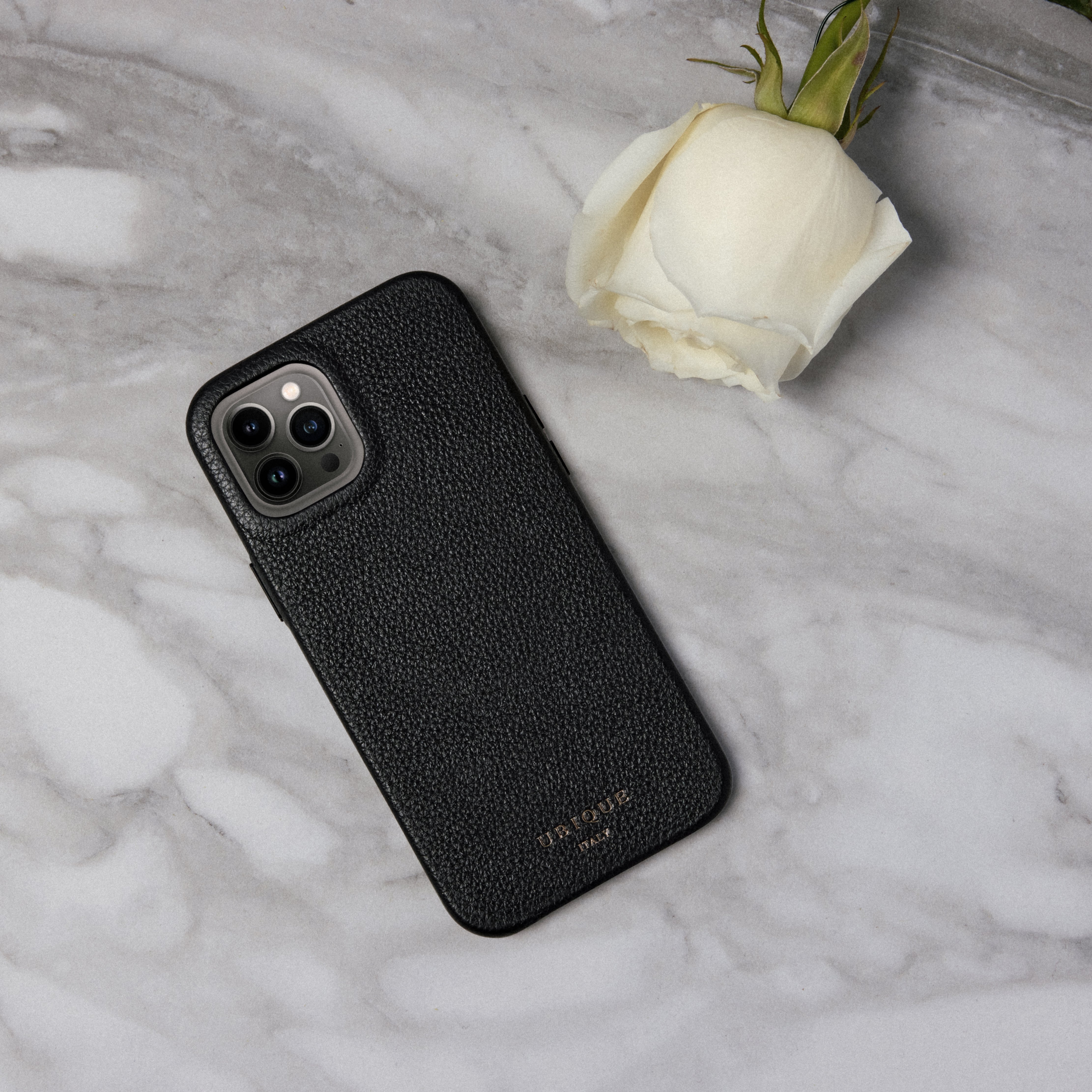 Black leather iPhone case on a white marble background with a white rose