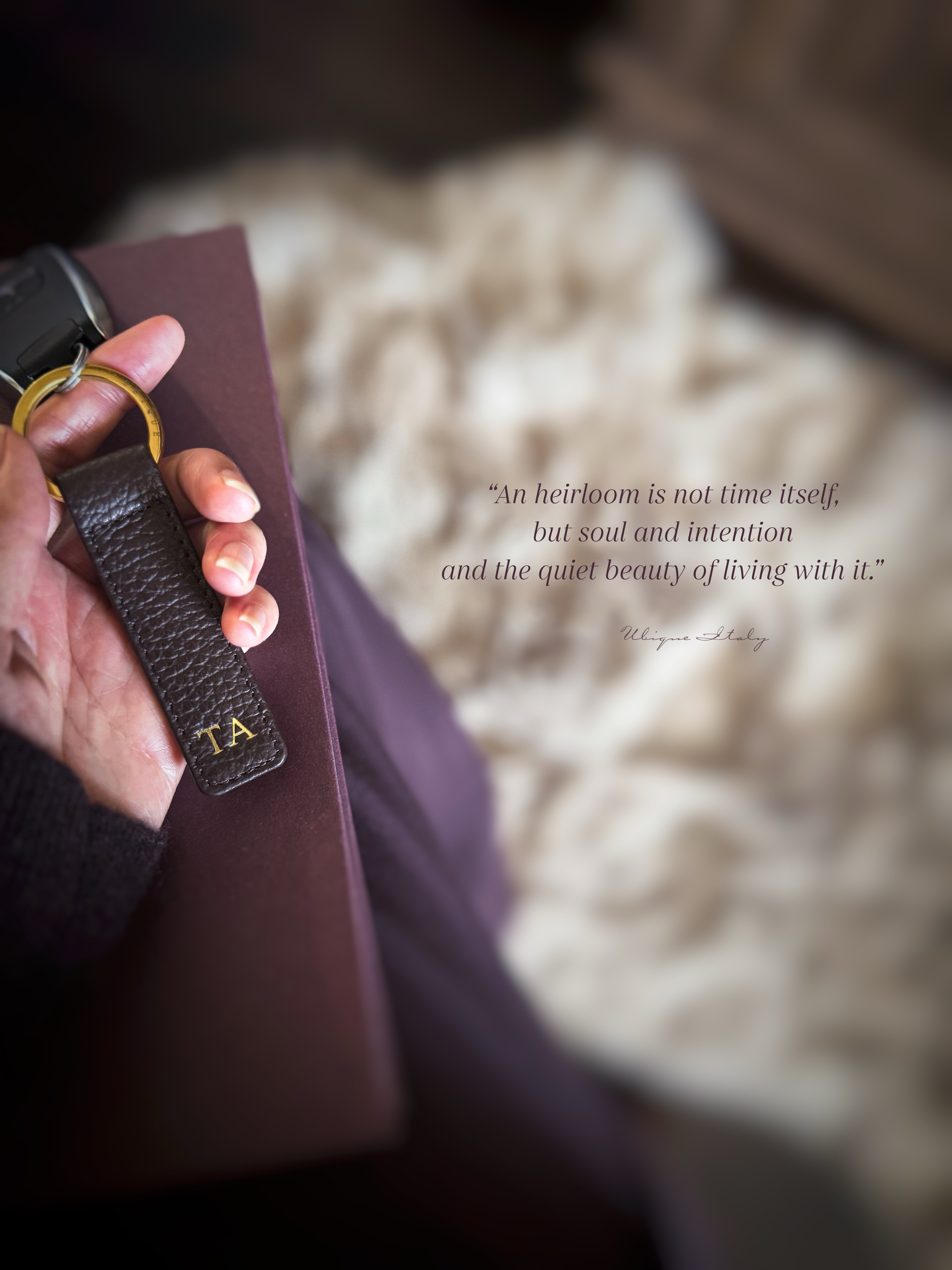 Hand holding a brown leather-bound book with a handcrafted leather keychain, blurred background with text overlay.